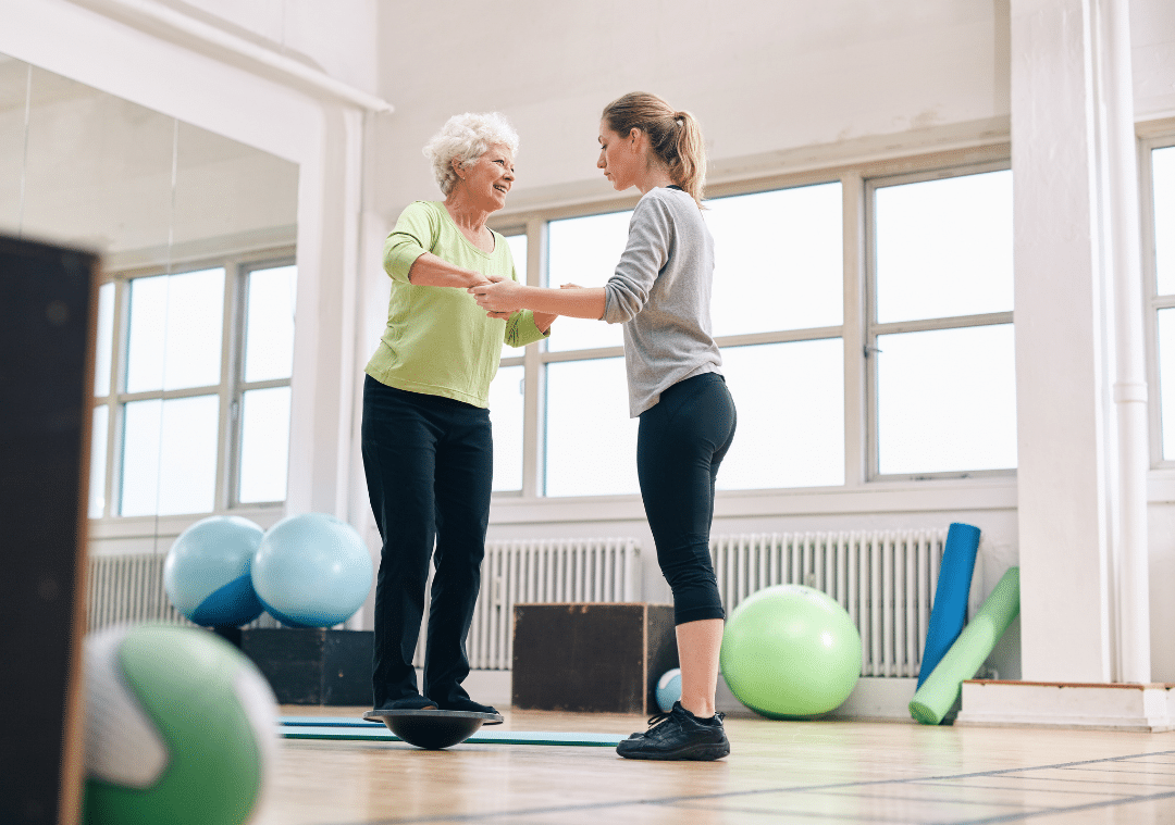 Instructor assisting an elderly woman balancing on a stability disc
